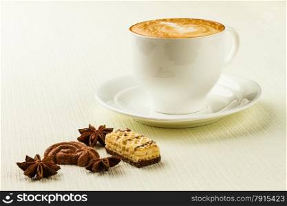 porcelain cup of cappucino, sweet and spices on white background
