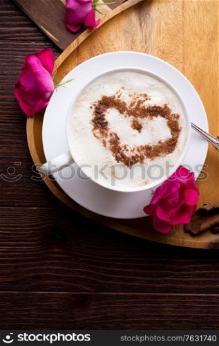 porcelain cup of coffee with ice cream and cinnamon heart served at black wooden table with pink roses. life style concept