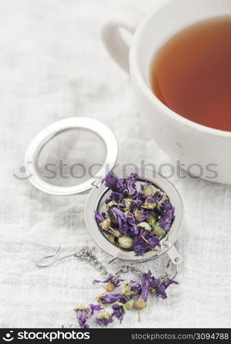 Porcelain cup with hot tea and infuser with loose blue mallow tea on white kitchen towel