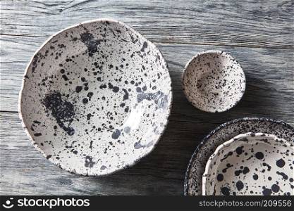 Porcelain gray bowls and plates on a gray wooden table with place for text. Colorful ceramic vintage handmade dishes. Flat lay. Decorative pottery - bowls, plates covered with glazed on a gray wooden background. Top view of traditional handcrafted.