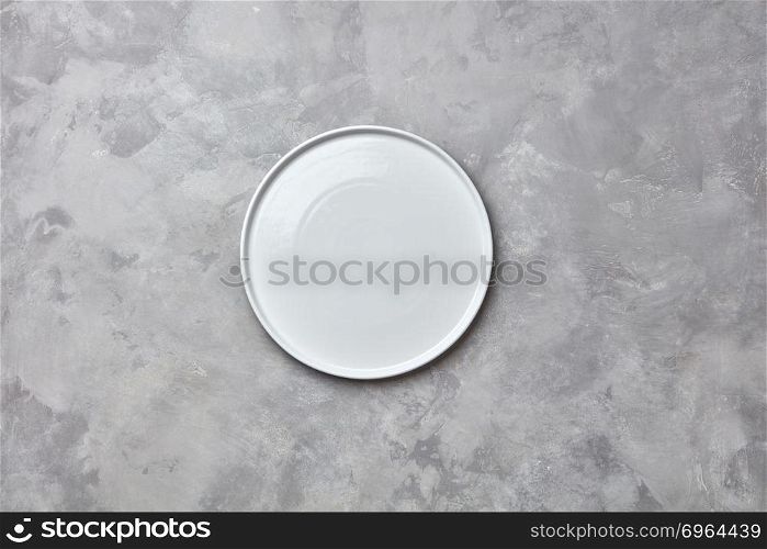 Porcelain handmade empty round a plate on a gray concrete background with a copy of space. Can be used for display or montage your products. Flat lay. Decorative ceramic empty white handmade plate presented on a gray concrete background with copy space for your menu. Flat lay