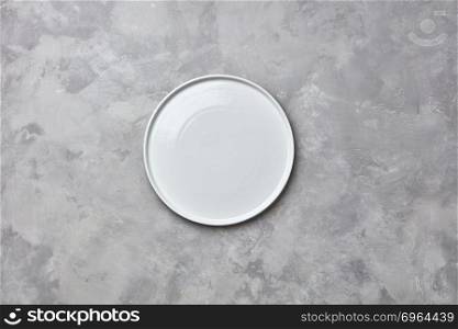 Porcelain handmade empty round a plate on a gray concrete background with a copy of space. Can be used for display or montage your products. Flat lay. Decorative ceramic empty white handmade plate presented on a gray concrete background with copy space for your menu. Flat lay