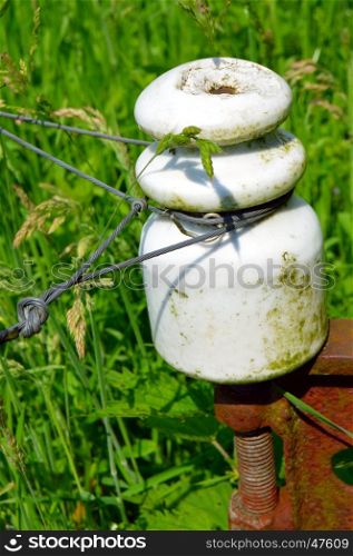 Porcelain insulator on a metal picket with barbed wires.
