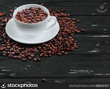 Porcelain white coffee cup and beans on black shabby wooden background. Top view.. Porcelain white coffee cup and roasted beans on black shabby wooden background. Top view.