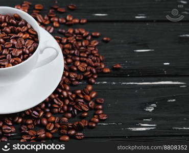 Porcelain white coffee cup and beans on black shabby wooden background. Top view.. Porcelain white coffee cup and roasted beans on black shabby wooden background. Top view. Copy space.