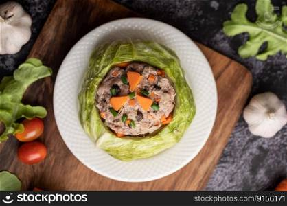 Pork cabbage soup with carrots, chopped green onions, cucumber in a wooden plate on a wooden plate.