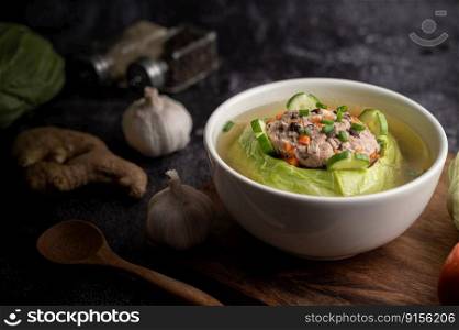 Pork cabbage soup with carrots, chopped green onions, cucumber in a wooden plate on a wooden plate.