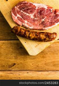 Pork chops with condiments and smoked sausage on a wooden cutting board over wooden table, meat for bbq, top view, copy space, barbeque concept