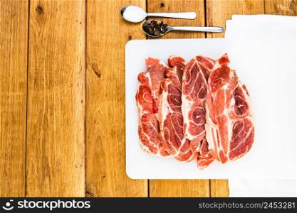 Pork chops with condiments on a white cutting board over wooden table, meat for bbq, top view, copy space, barbeque concept