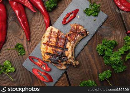 pork fried steak on the rib lies on a black board, next to fresh red chili peppers, top view