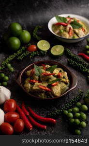 Pork green curry in a brown bowl with spices on a black cement background