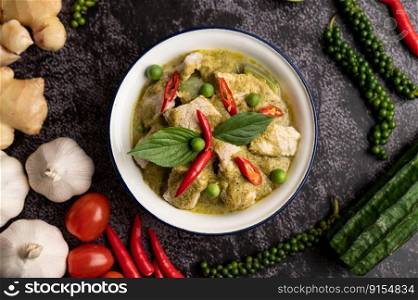 Pork green curry in a white bowl with spices on a black cement background
