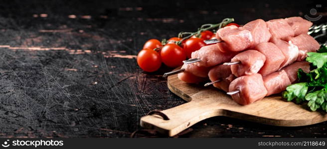 Pork kebab raw on a cutting board with tomatoes and herbs. Against a dark background. High quality photo. Pork kebab raw on a cutting board with tomatoes and herbs.