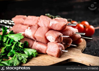 Pork kebab raw on a cutting board with tomatoes and herbs. Against a dark background. High quality photo. Pork kebab raw on a cutting board with tomatoes and herbs.