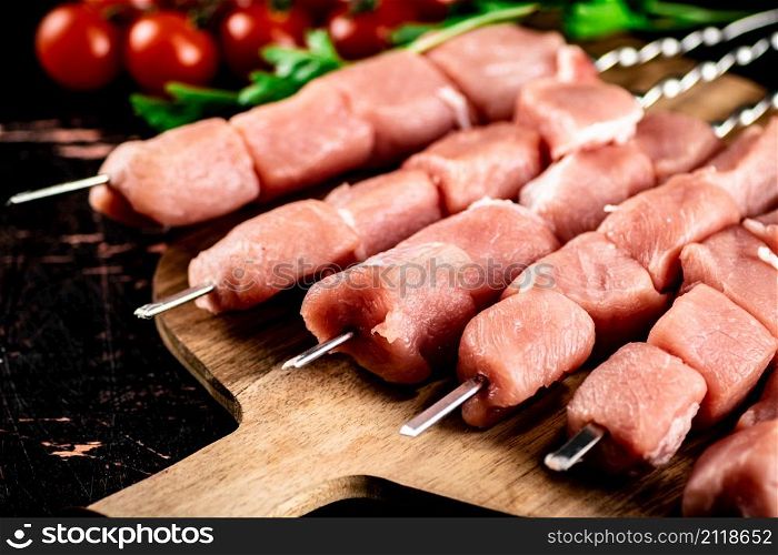 Pork kebab raw on a cutting board with tomatoes and herbs. Against a dark background. High quality photo. Pork kebab raw on a cutting board with tomatoes and herbs.