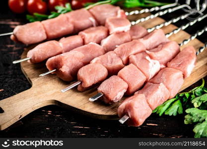 Pork kebab raw on a cutting board with tomatoes and herbs. Against a dark background. High quality photo. Pork kebab raw on a cutting board with tomatoes and herbs.