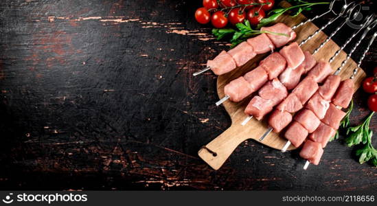 Pork kebab raw on a cutting board with tomatoes and herbs. Against a dark background. High quality photo. Pork kebab raw on a cutting board with tomatoes and herbs.