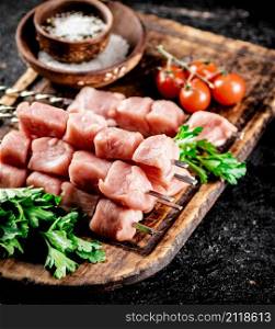 Pork kebab raw on a cutting board with tomatoes and parsley. On a black background. High quality photo. Pork kebab raw on a cutting board with tomatoes and parsley.