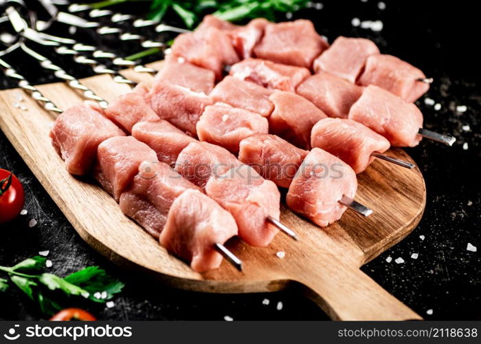 Pork kebab raw on a cutting board with tomatoes and parsley. On a black background. High quality photo. Pork kebab raw on a cutting board with tomatoes and parsley.