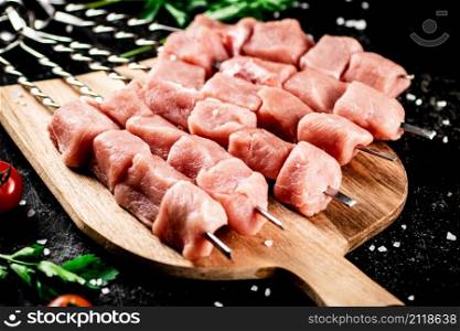 Pork kebab raw on a cutting board with tomatoes and parsley. On a black background. High quality photo. Pork kebab raw on a cutting board with tomatoes and parsley.