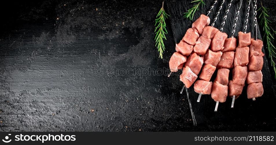 Pork kebab raw on a stone board with rosemary. On a black background. High quality photo. Pork kebab raw on a stone board with rosemary.