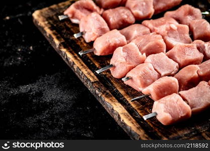 Pork kebab raw on a wooden cutting board. On a black background. High quality photo. Pork kebab raw on a wooden cutting board.