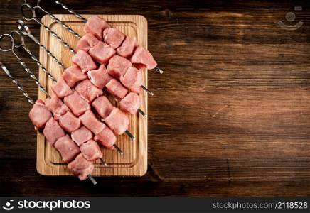 Pork kebab raw on skewers on a cutting board. On a wooden background. High quality photo. Pork kebab raw on skewers on a cutting board.