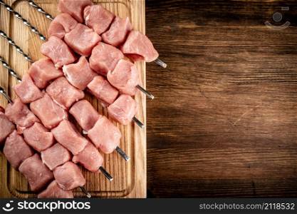 Pork kebab raw on skewers on a cutting board. On a wooden background. High quality photo. Pork kebab raw on skewers on a cutting board.