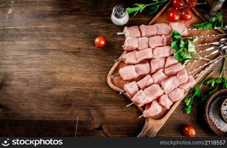 Pork kebab raw on skewers with parsley and tomatoes on a cutting board. On a wooden background. High quality photo. Pork kebab raw on skewers with parsley and tomatoes on a cutting board.