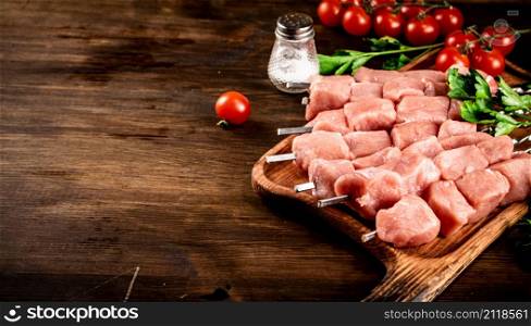 Pork kebab raw on skewers with parsley and tomatoes on a cutting board. On a wooden background. High quality photo. Pork kebab raw on skewers with parsley and tomatoes on a cutting board.
