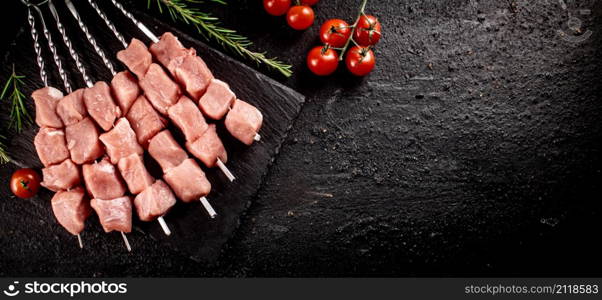 Pork kebab raw with tomatoes on a stone board. On a black background. High quality photo. Pork kebab raw with tomatoes on a stone board.