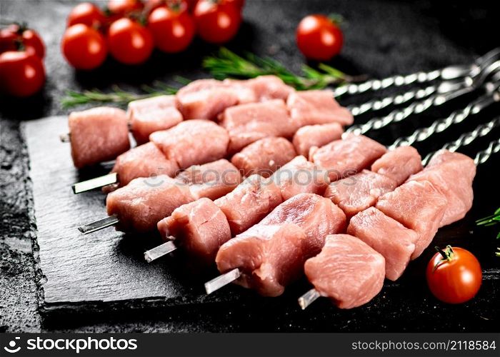 Pork kebab raw with tomatoes on a stone board. On a black background. High quality photo. Pork kebab raw with tomatoes on a stone board.
