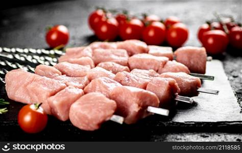 Pork kebab raw with tomatoes on a stone board. On a black background. High quality photo. Pork kebab raw with tomatoes on a stone board.