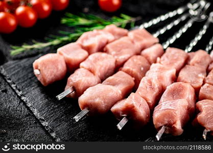 Pork kebab raw with tomatoes on a stone board. On a black background. High quality photo. Pork kebab raw with tomatoes on a stone board.