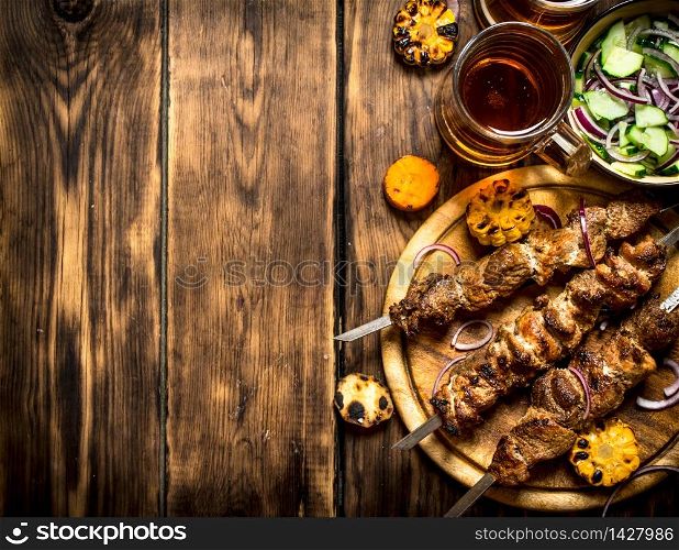Pork kebab with beer and vegetables. On wooden background.. Pork kebab with beer and vegetables.