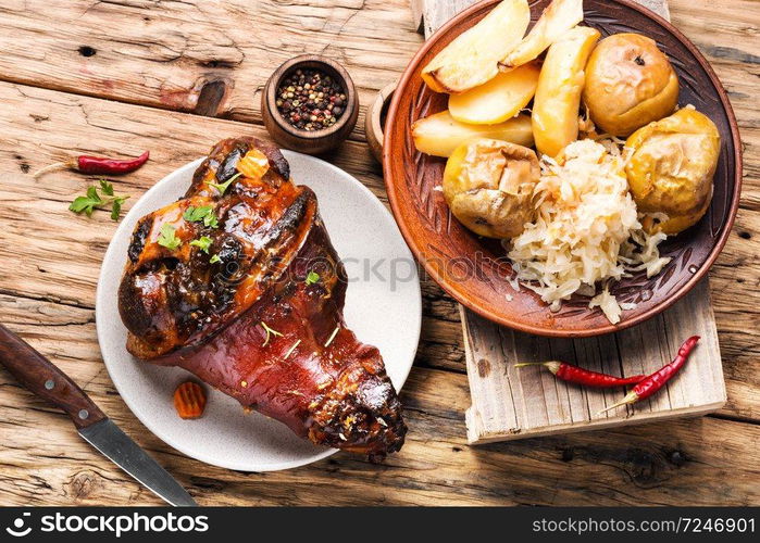 Pork knuckle on rustic table.Roasted pork knuckle with potatoes. Pork knuckle with fried sauerkraut