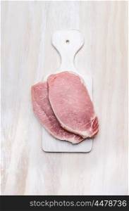 pork loin fillet meat on white cutting board over wooden background, top view
