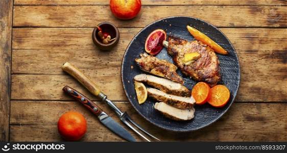 Pork on the bone baked in oranges, lime and tangerine. Meat in the plate on wooden table. Barbecue meat steak with citrus fruits.