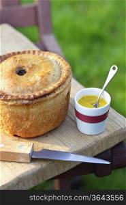 Pork pie, knife and cup of mustard on table outdoors