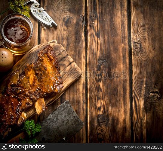 Pork ribs grilled with a meat hatchet and beer. On a wooden table.. Pork ribs grilled with a meat hatchet and beer.