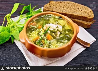 Pork ribs soup with couscous and spinach in a clay bowl on napkin, bread on dark wooden board background