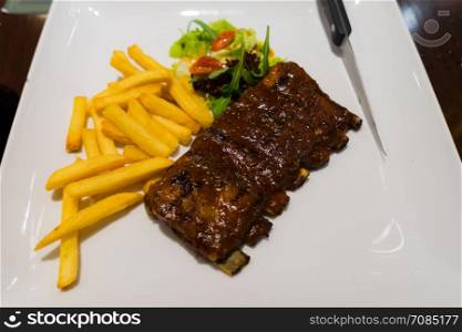 Pork ribs steak fries and vegetables on white plate, Roasted sliced barbecue pork ribs, focus on sliced meat