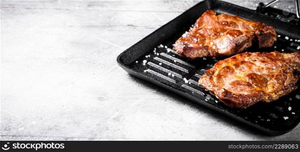 Pork steak in a grill pan. On a gray background. High quality photo. Pork steak in a grill pan.
