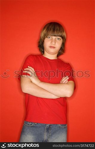 Portait of Caucasian boy with arms crossed standing against red background.