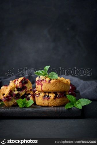 Portion crumble pie with cherries on a wooden board decorated with green mint leaves, black background