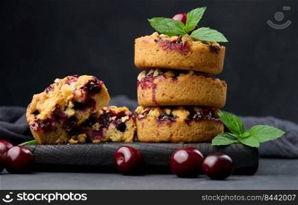 Portion crumble pie with cherries on a wooden board decorated with green mint leaves, black background