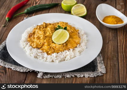 Portion of chicken curry garnished with rice and fresh lime 
