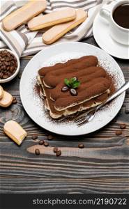 portion of Classic tiramisu dessert, cup of coffee and milk or cream on wooden background or table. portion of Classic tiramisu dessert, cup of coffee and milk or cream on wooden background