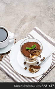 Portion of Classic tiramisu dessert in a glass and cup of coffee on concrete background or table. Portion of Classic tiramisu dessert in a glass and cup of coffee on concrete background