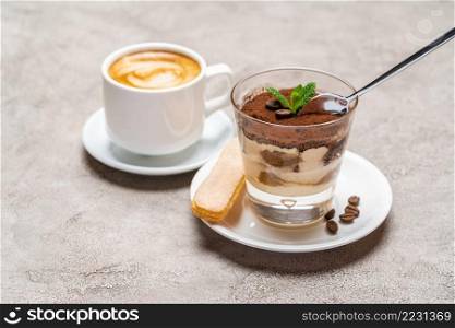 Portion of Classic tiramisu dessert in a glass cup and espresso coffee on concrete background or table. Portion of Classic tiramisu dessert in a glass cup and espresso coffee on concrete background